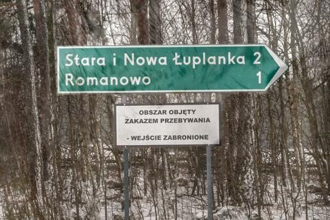 Drogowskaz z umieszczoną pod spodem białą tablicą z napisem: Obszar objęty zakazem przebywania - wejście zabronione