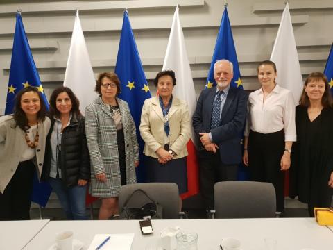 Siedem osób - uczestników spotkania - pozuje do zdjęcia na tle flag Polski i Unii Europejskiej. W centrum kadru stoi zastępczyni RPO Hanna Machińska