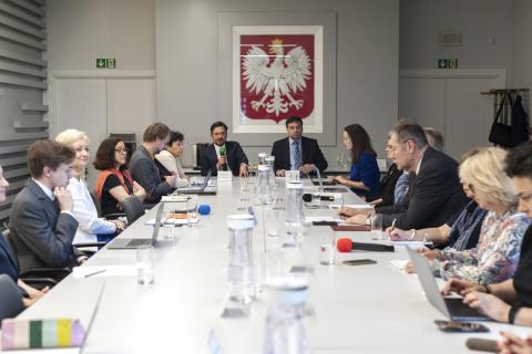 Kilkanaście osób siedzących przy stole konferencyjnym