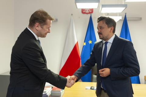 RPO Marcin Wiącek ściska dłoń prezesa Okręgowej Izby Lekarskiej w Warszawie Piotra Pawliszaka na powitanie na tle flag Polski i UE