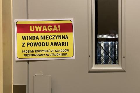 Drzwi windy z przyklejoną kartką z napisem "Winda nieczynna z powodu awarii. Prosimy korzystać ze schodów. Przepraszamy za utrudnienia"