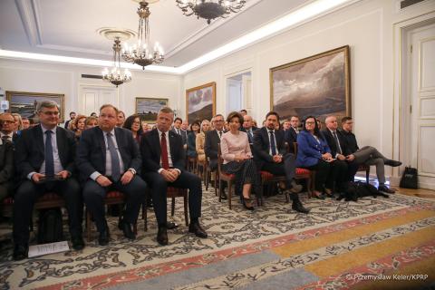 Kilkadziesiąt osób siedzi na krzesłach w dużej zabytkowej sali