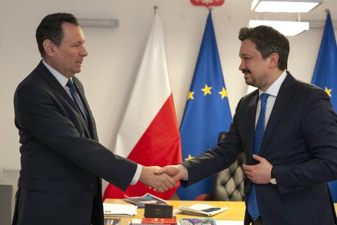 Dwie osoby ściskają dłonie na powitanie na tle flag Polski i UE