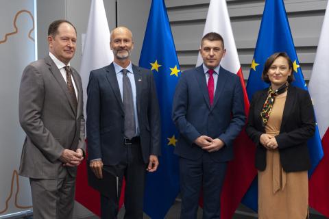 Cztery osoby pozują na stojąco do zdjęcia na tle flag Polski i UE