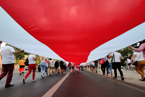 osoby niosą wielką flagę podczas manifestacji 