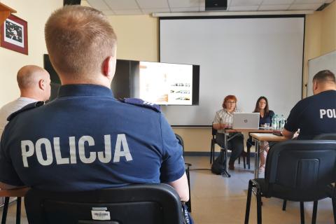 Kilkanaście osób na salce konferencyjnej słucha wystąpienia, na pierwszym planie siedzi osoba w mundurze z napisem POLICJA