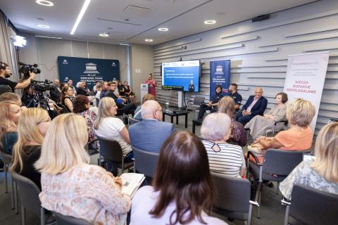 Kilkadziesiąt osób na sali konferencyjnej słucha wystąpienia o ogląda prezentację wyświetlaną na ekranie