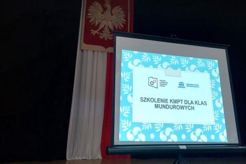 Ekran do projektora z grafiką z napisem "Szkolenie KMPT dla uczniów klas mundurowych"