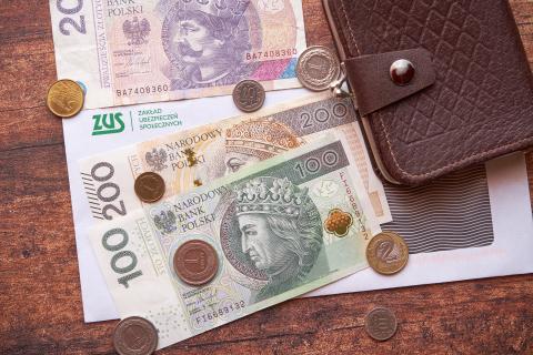 Portfel, banknoty i monety leżące na kopercie z nadrukowanym logiem Zakładu Ubezpieczeń Społecznych