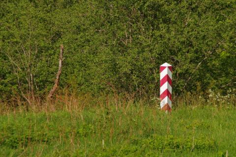 Słup w biało czerwone pasy stojący pośród traw i krzewów