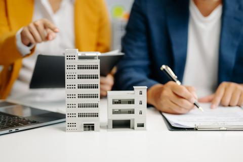 Dwie osoby notują przy biurku, na którym stoją makiety dwóch budynków