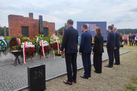 Pięć osób stoi i oddaje hołd przed wieńcami leżącymi przy pomniku