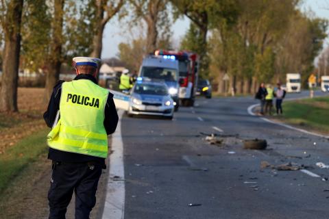 Policjant w zielonej kamizelce ogląda miejsce kolizji drogowej na ulicy