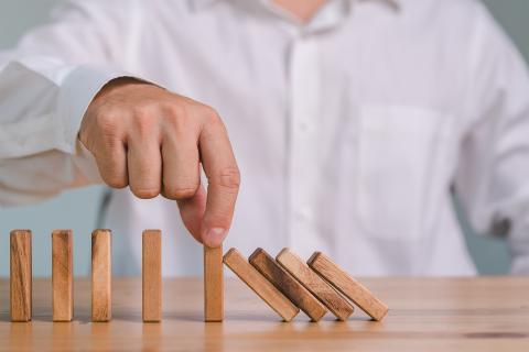 Mężczyzna powstrzymuje domino trzymając palcami drewniany klocek, na którym oparte są powalone wcześniej klocki