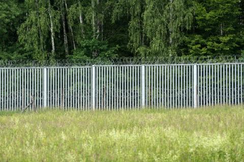 metalowa zapora graniczna na łące z lasem w tle 