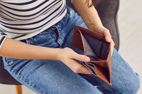 Siedząca na krześle kobieta zagląda do pustego portfela