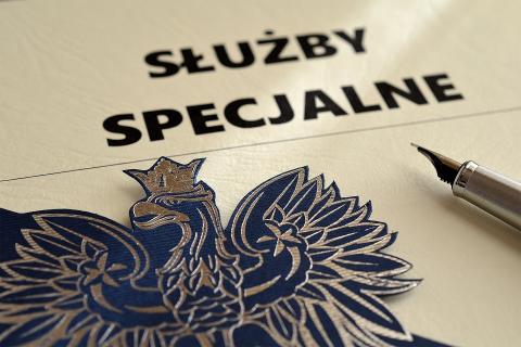 Ilustracja przedstawiająca papier z nadrukowanym napisem "służby specjalne", na którym leżą pióro i wycięty kontur godła Polski