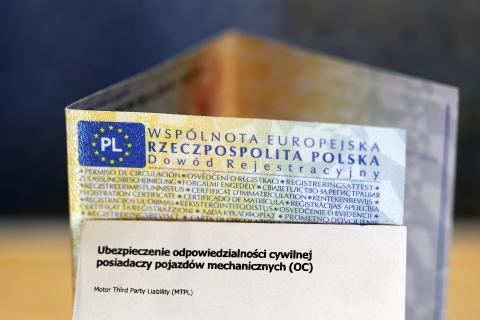 Zbliżenie na ustawiony na biurku blankiet polskiego dowodu rejestracyjnego pojazdu i kartonik z napisem "Ubezpieczenie odpowiedzialności cywilnej posiadaczy pojazdów mechanicznych (OC)"