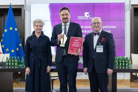 Marcin Wiącek, Beata Małecka-Libera oraz Henryk Skarżyński pozują do zdjęcia uśmiechając się. Marcin Wiącek trzyma w dłoniach statuetkę i dyplom nagrody.