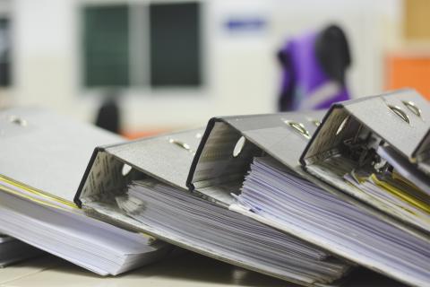 Leżące na biurku cztery segregatory zapełnione dokumentami