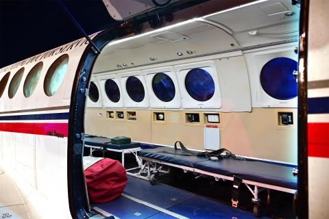 Otwarty właz samolotu, w środku którego znajduje sie kilka łóżek do transportu pacjentów