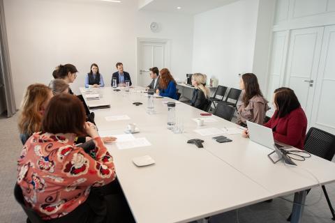 Kilkanaście osób siedzi przy podłużnym stole w sali konferencyjnej