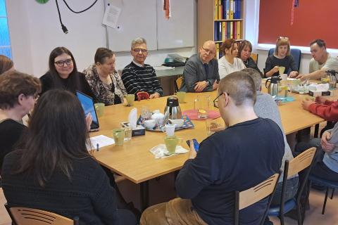 Kilkanaście osób siedzi wokół dużego stołu i rozmawia