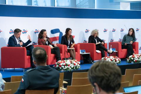 Pięć osób siedzi na fotelach na podwyższeniu w sali konferencyjnej