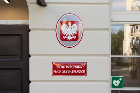Czerwona tablica z napisem "Biuro Rzecznika Praw Obywatelskich" oraz tablica z polskim godłem narodowym wisząca nad nią