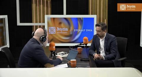 Dwie osoby siedzą obok siebie przy stole i rozmawiają, mówiąc do mikrofonów