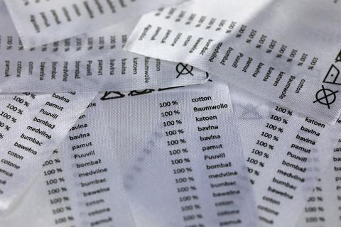 Stos metek, na których w wielu językach zapisana jest informacja o materiałowym składzie artykułu - 100% bawełna