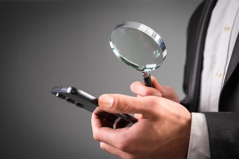 Mężczyzna w garniturze ogląda pod lupą telefon komórkowy