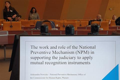 Sala konferencyjna z ekranem, na którym widać tytuł wygłaszanego referatu w języku angielskim