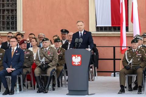 osoba przemawia na stojąco, słuchają jej osoby siedzące 