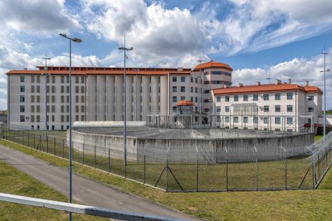 Widok ogólny kompleksu budynków więziennych - wielopiętrowy budynek z kratami w oknach otoczony ogrodzeniem zakończonym drutem kolczastym