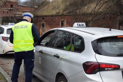 Policjant w mundurze stoi obok samochodu osobowego ze znakiem "TAXI" umieszczonym na dachu.
