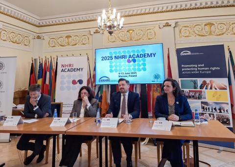 Cztery osoby siedzą przy stole prezydialnym. W tle widać ekran wyświetlający nazwę "2025 NHRI Academy"