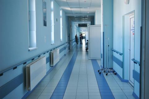 Ogólny widok długiego korytarza w szpitalu. Na końcu korytarza stoi rozmawiająca grupa ludzi
