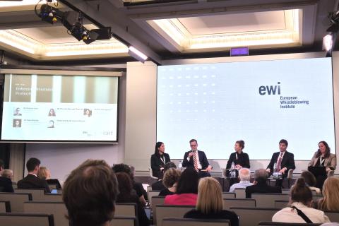Pięć osób siedzi na scenie sali konferencyjnej na tle wyświetlacza z napisem "EWI - European Whistleblowing Instytite", kilkadziesiąt osób słucha wystąpień