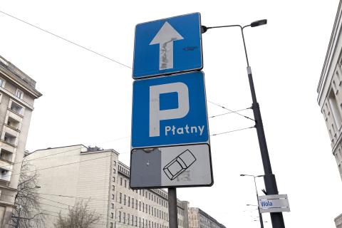 drogowy znak parkingu z dopiskiem "płatny" na tle domów