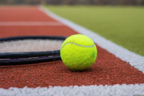 Rakieta i piłka tenisowa leżą na korcie tenisowym