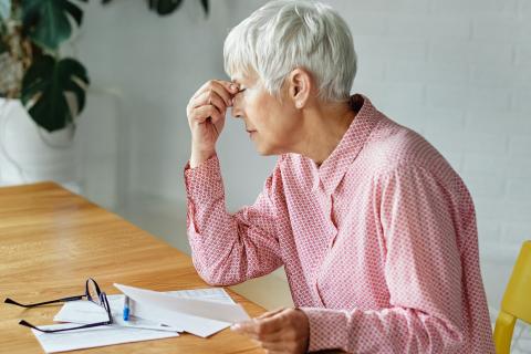 starsza pani siedzi za stołem dotykając dłonią głowy  