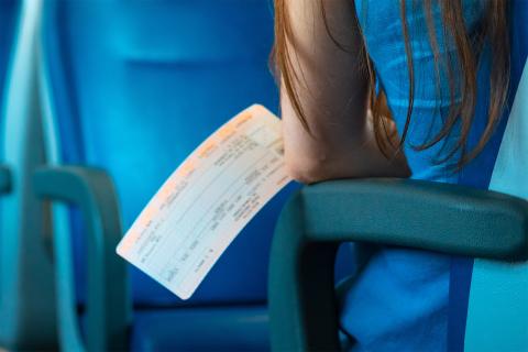 Siedząca w fotelu w wagonie bezprzedziałowym osoba trzyma w dłoni bilet pociągowy