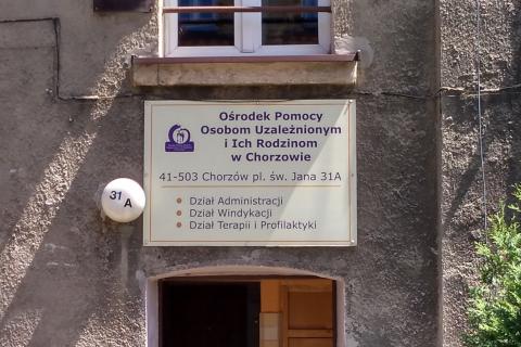 Tablica z napisem "Ośrodek Pomocy Osobom Uzależnionym i Ich Rodzinom w Chorzowie" na elewacji budynku
