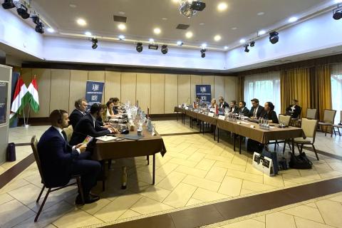 Kilkanaście osób siedzi po dwóch stronach stołów w sali konferencyjnej