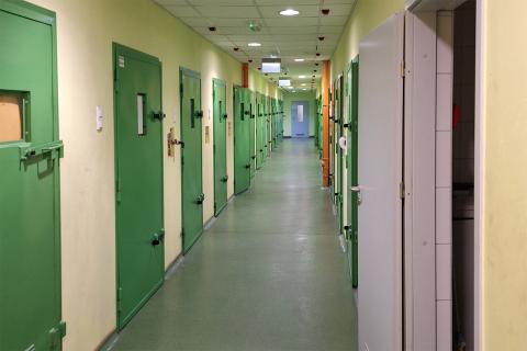 Zdjęcie przedstawiające szereg wzmacnianych, stalowych drzwi w długim korytarzu. W drzwiach są niewielkie okienka.