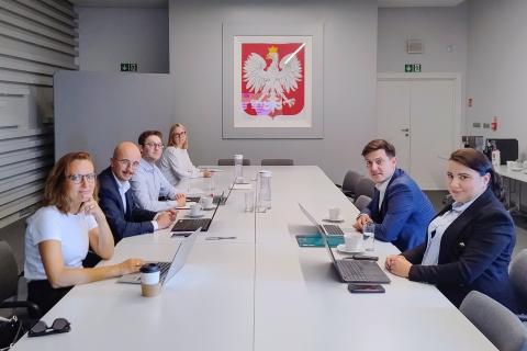 Sześć osób siedzi przy stole konferencyjnym i uśmiecha się, pozując do zdjęcia