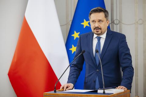 RPO Marcin Wiącek wypowiada się stojąc przy mównicy w sali posiedzeń Senatu. Za nim znajdują się flagi Polski i Unii Europejskiej