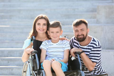 Rodzina - kobieta, mężczyzna i chłopiec siedzący na wózku - uśmiechają się pozując do zdjęcia
