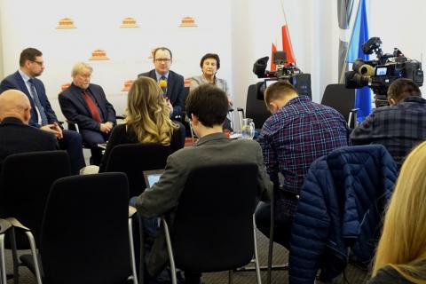 zdjęcie: trzej mężczyźni i koebiat siedzą na krzesłach przed nimi stoją dwie kamery i siedzi kilka osób